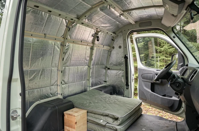 Isolation thermique légère en mousse alvéolaire revêtement aluminium installée sur les parois et plafond d'un Peugeot Expert aménagé travail-bivouac, matelas et caisse bois visibles